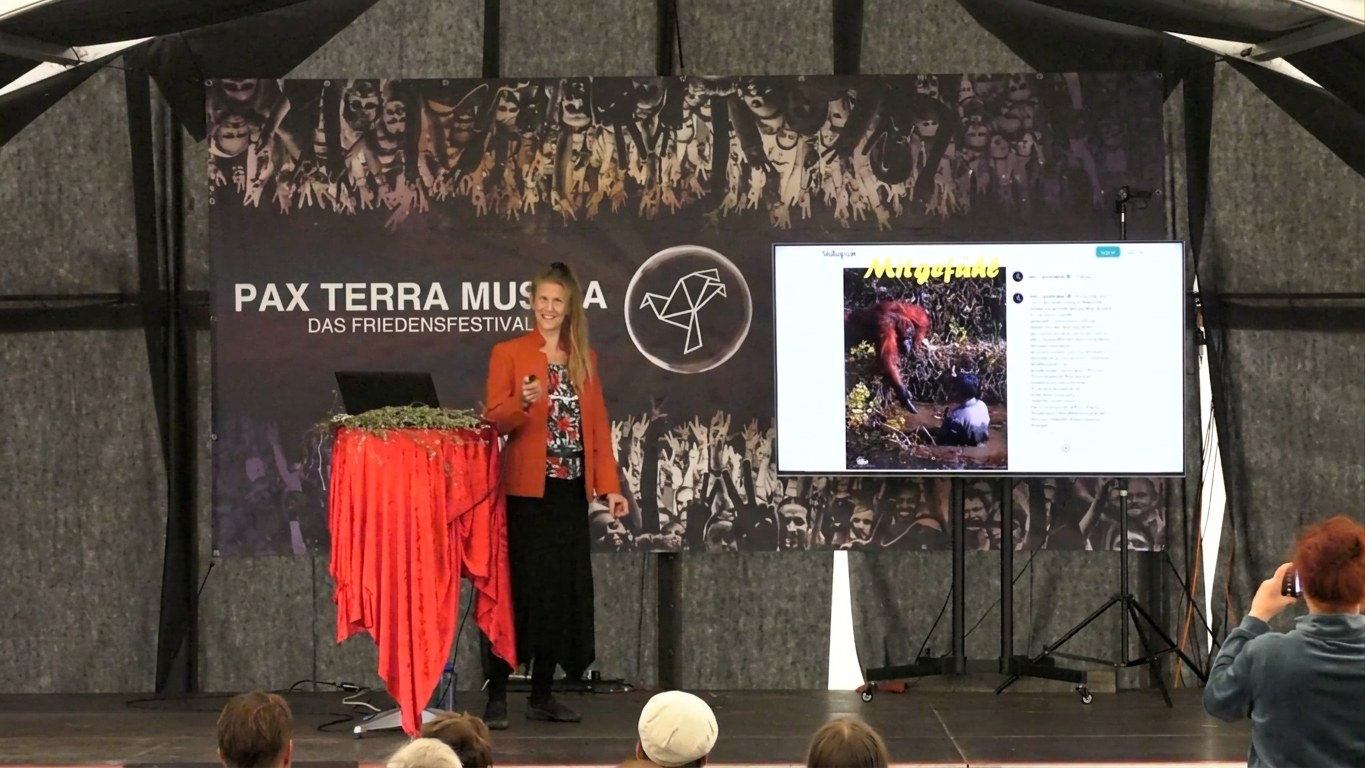 Angela Mahr hält auf der Bühne des Friedensfestivals Pax Terra Musica einen Vortrag, im Vordergrund das Publikum